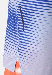 Tissu à rayures bleues et blanches avec une couture verticale et une fente latérale laissant apparaître un tissu orange en dessous.