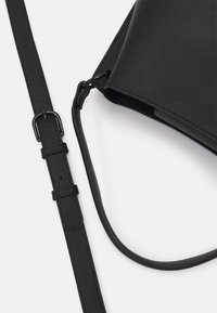 Zwarte schoudertas in gestructureerd faux leer, met een afneembare riem en een minimalistisch ontwerp. Eenvoudige hardware accenten maken de look compleet.