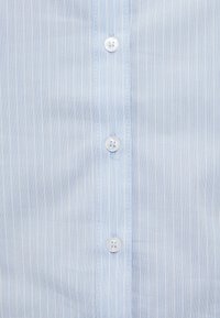 Ανοιχτό μπλε πουκάμισο με κάθετες λεπτές ρίγες σε λευκό, έξι λευκά κουμπιά μπροστά και απαλό ύφασμα με υφή.