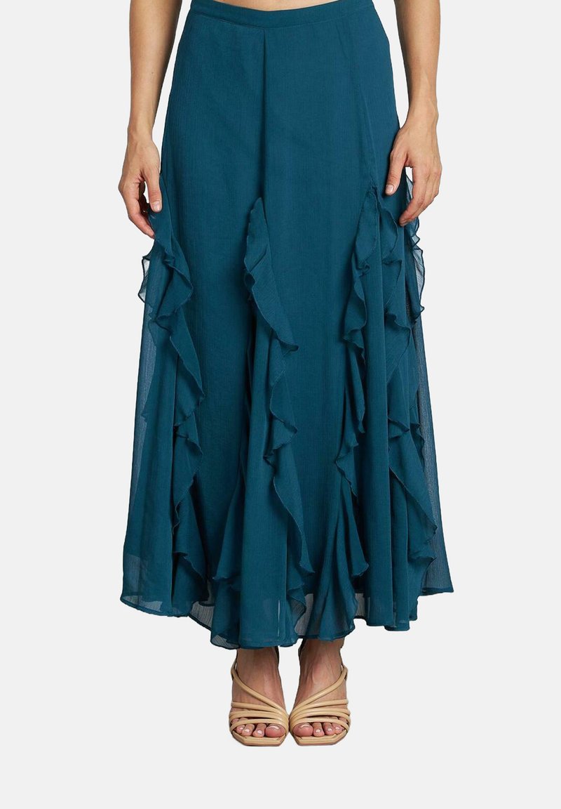 Gonna maxi fluida color teal con strati di rouches lungo l'orlo e una vita. Abbinata a sandali con cinturino nude. Tessuto leggero.