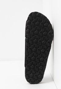 Suola di scarpa in gomma nera con superficie testurizzata, caratterizzata da un motivo di forme circolari sollevate per migliorare la trazione. Visto di lato su uno sfondo bianco.