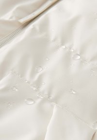 Tessuto bianco impermeabile con una superficie liscia, caratterizzato da gocce d'acqua sulla superficie e una cerniera visibile lungo un lato.