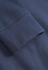Mørkeblå sweatshirt-stof med ribbet manchet, der har en glat overflade og pæne sting. Manchetten er foldet tilbage, hvilket afslører rene linjer.