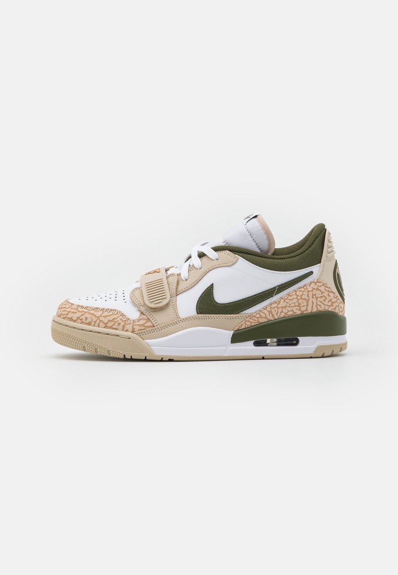 Nike sneaker with a white leather upper, green accents, beige and patterned rubber sole, and adjustable strap across the midfoot.