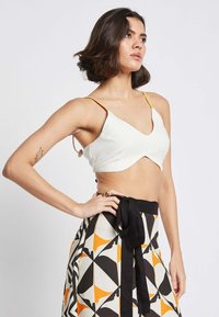 White crop top with adjustable yellow straps, featuring a V-neck and a sleek design. Paired with a patterned skirt in black, orange, and cream.