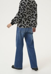 Pull gris avec imprimé léopard noir, coupe ample et poignets côtelés, associé à un jean denim bleu ample avec poches arrière et texture délavée.