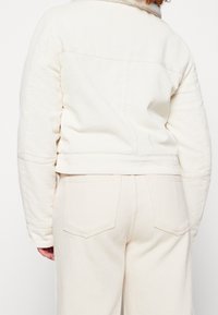 White corduroy jacket with a short fit and ribbed texture, featuring a collar and back seam detail, paired with matching trousers.