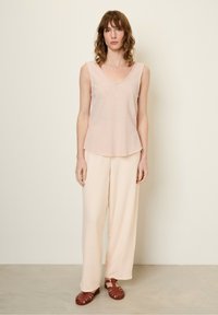 Jasnoróżowy top na ramiączkach z okrągłym dekoltem, połączony z luźnymi, jasnobeżowymi spodniami i brązowymi sandałami na paski. Gładka tekstura, swobodny krój.