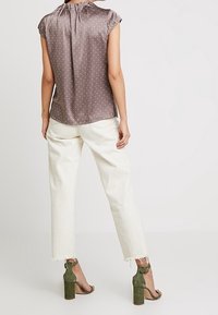 Bruine blouse met stippen en korte mouwen; gecombineerd met witte broeken met een rafelrand en olijfgroene hoge hakken. Soepele textuur, casual uitstraling.