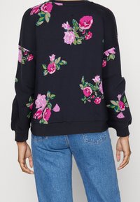 Sweat-shirt bleu marine avec imprimés floraux roses et violets porté avec un jean bleu, vu de dos.