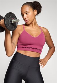 Under Armour sports-bh i dyp rosa med tynne stropper, med et svart logobånd; kombinert med høyhalsede svart leggings.