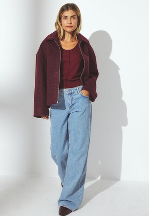 Giacca in misto lana bordeaux con zip, camicia bordeaux con bottoni, jeans a gamba larga azzurri chiari e scarpe marrone scuro. Vestibilità semplice e rilassata.