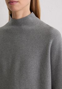Grauer Pullover mit hohem Kragen aus glattem Strickstoff, der eine lässige Passform und minimale Nahtdetails aufweist.