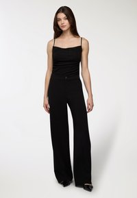 Czarna dopasowana kamizelka na cienkich ramiączkach, zestawiona z czarnymi spodniami o szerokich nogawkach z wysokim stanem, z zapięciem na guziki i gładką teksturą.