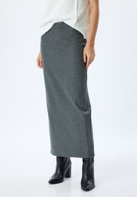 Gonna maxi in grigio scuro, realizzata in tessuto morbido, presenta una vita aderente e cade dritta fino alle caviglie, abbinata a stivali neri con tacco.