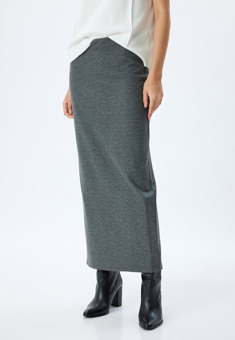 Jupe maxi gris foncé, en tissu doux, dotée d'une taille cintrée et tombant droit jusqu'aux chevilles, associée à des bottes à talons noires.