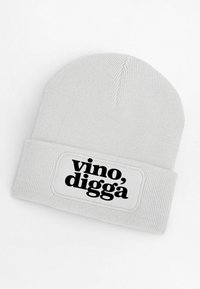 White knitted beanie with a turned-up cuff featuring a rectangular label that displays the text "vino, diggà" in bold black font.