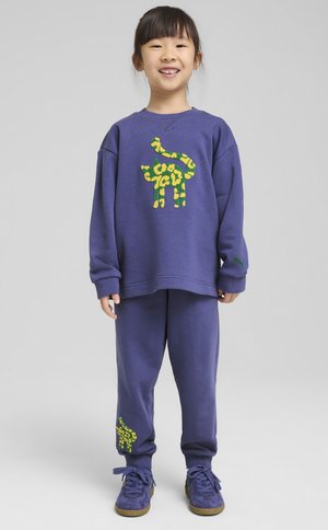 Conjunto de sudadera y pantalones de chándal morados con un diseño de jirafa verde y amarilla en la parte delantera y lateral. Material de algodón suave, corte relajado.
