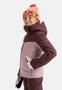 Paarse en kastanjebruine skijas met capuchon, voorzien van een ritssluiting en Roxy-logo. Oranje gebreide beanie met patroon. Handschoenen met geometrisch ontwerp.
