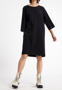 Czarna sukienka o luźnym kroju, okrągłym dekolcie i rękawach do trzy czwarte, w zestawieniu z beżowymi botkami na kostkę z lace-up i masywną podeszwą.