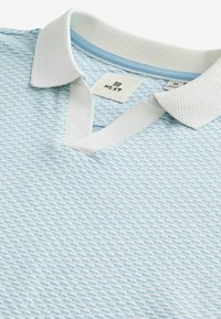 Vaaleansininen poolopaita, jossa on teksturoitu kuvio, valkoinen kaulus ja nappilista. Koko M, hengittävästä materiaalista valmistettu.