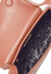 Brązowa skórzana torebka o gładkiej teksturze, z złotym akcentem w wewnętrznej kieszeni oraz czarną satynową podszewką.