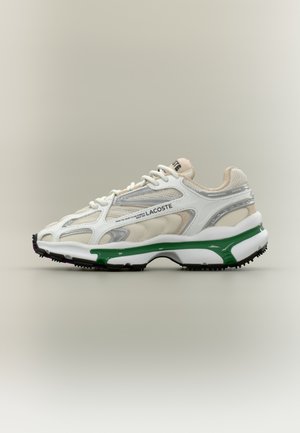 Le sneaker Lacoste presenta una parte superiore in rete bianca con accenti argento e verde, dettagli testurizzati e una suola in gomma nera con evidenziature viola.