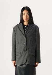 Stribet blazer i antrasittgrå, strukturert form, to frontlommer, fem knapper, utskårne reverser, parret med en svart topp under.