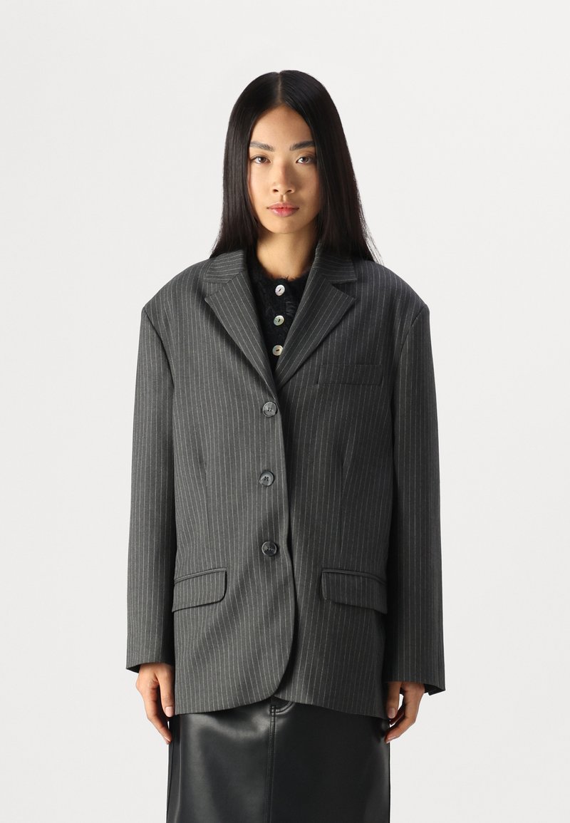 Stribet blazer i antrasittgrå, strukturert form, to frontlommer, fem knapper, utskårne reverser, parret med en svart topp under.