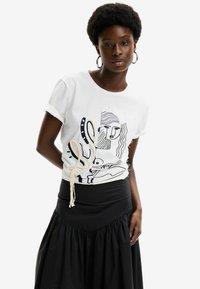 Camiseta de algodón blanca con diseños en arte lineal negro y un detalle de cuerda en el lateral, combinada con una falda negra de tela recogida.