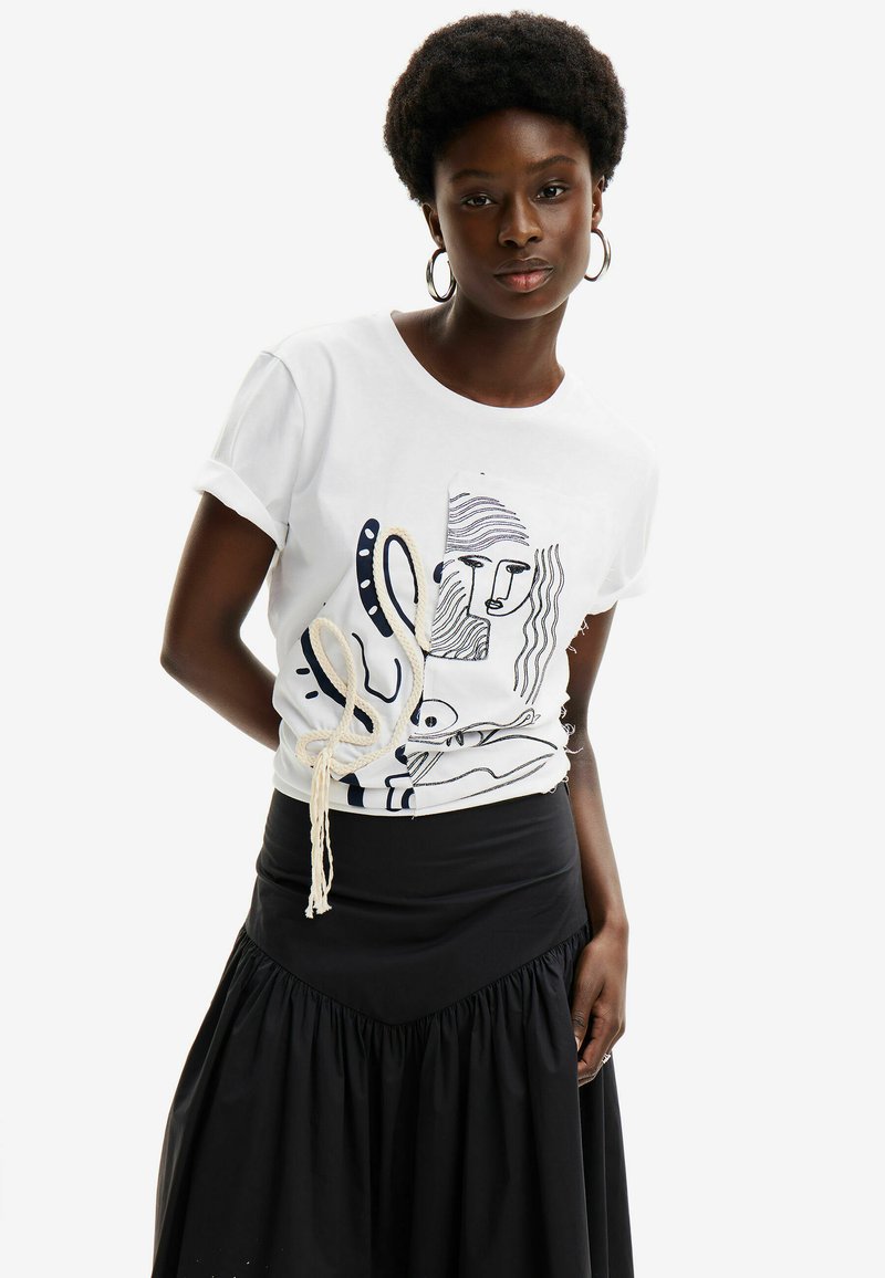 Camiseta de algodón blanca con diseños en arte lineal negro y un detalle de cuerda en el lateral, combinada con una falda negra de tela recogida.