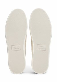Teksturowane beżowe podeszwy butów z białymi gumowymi podeszwami zewnętrznymi. Z wygrawerowanym logo "TOMMY HILFIGER" w okolicy pięty.
