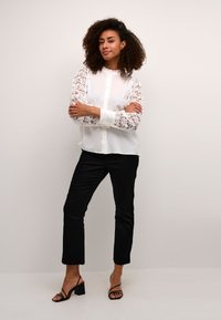 White blouse with lace long sleeves, button-down front; paired with black tailored pants and strappy black heels.