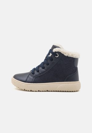Baskets montantes bleu marine avec semelle beige et doublure en polaire blanche, lacets à l'avant, conçues pour temps froid.