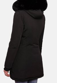 Veste matelassée noire avec capuche et col en fausse fourrure. Comprend des poches latérales et des poignets côtelés, avec une texture extérieure lisse.