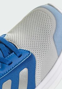 Chaussure de sport bleue et argentée avec tissu en maille, accents en cuir et surface texturée, dotée d'un orteil arrondi et de coutures contrastées.