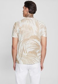 Trumpas rankovėmis marškinis, pagamintas iš lengvos medžiagos, su kreminiu pagrindu ir subtiliais smėlio spalvos palmės lapų raštais. Paprasta nugarėlė, su laisvu kirpimu.