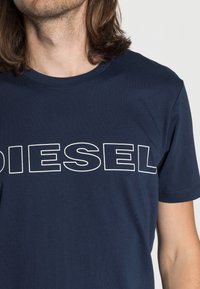Námořnická modrá bavlněná tričko s velkým bílým logem "DIESEL" přes hruď; kulatý výstřih a krátké rukávy. Měkká struktura.