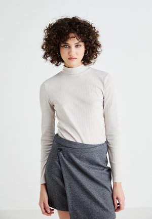 Lys beige ribbet turtleneck topp med lange ermer, kombinert med et grått herringbone omslagskjørt med en knappdetalj på siden.