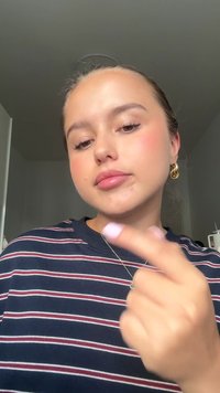 Modell trägt ein marineblau gestreiftes Hemd mit weißen und roten Linien, zeigt Creolen und eine Halskette und macht eine Handgeste.