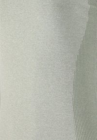 Ljusgrön topp med en slät framsida och en ribbad detalj på ena sidan, tillverkad av ett mjukt och stretchigt tyg.