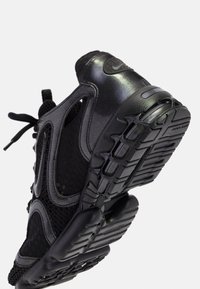 Baskets de sport noires avec côtés en mesh, semelle texturée et logo Nike visible, vues de l'arrière en angle et du dessous.