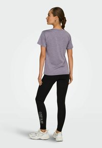 Paars T-shirt met korte mouwen en een ronde hals, gecombineerd met zwarte leggings met een logo-print op het onderbeen, gedragen met witte sneakers.