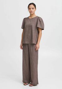 Top texturat maro cu mansete balon și pantaloni largi asortați. Dungi verticale subtile într-un material ușor. Sandale negre completează ținuta.