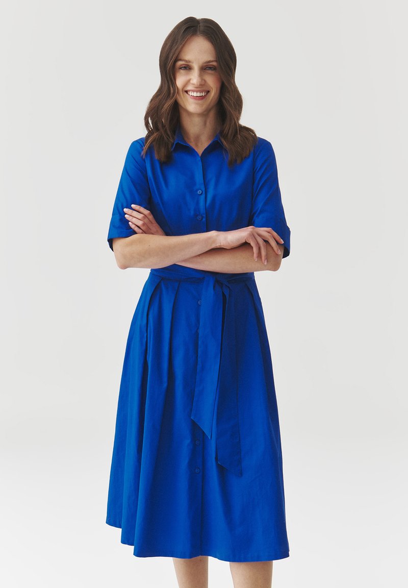 Blue button-up dress made of smooth fabric, featuring short sleeves, a tied waist, and a knee-length skirt with pleats.