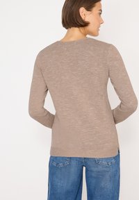 Maglia a maniche lunghe color khaki con scollatura a girocollo, caratterizzata da una finitura texturizzata e spacchi laterali. Abbinata a pantaloni blu a vita alta.