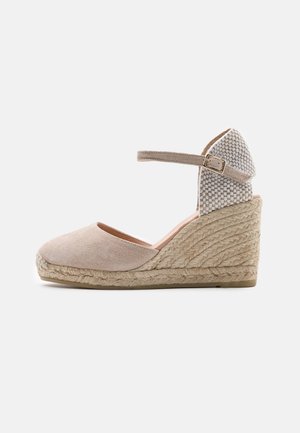 Espadrilles compensées en suède beige avec un talon en tissu tissé, une bride autour de la cheville et une semelle en corde de jute. Texture lisse avec un embout légèrement arrondi.