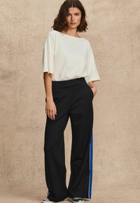 Ljus beige kortärmad topp i kombination med svarta vida byxor med blå sidostrikar. Outfiten har en avslappnad passform och en mjuk textur.
