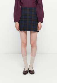 Geruite mini-rok met een blauw en bruin patroon, met een rechte snit en een voorknip, gecombineerd met beige sokken en glanzende bordeauxrode schoenen.