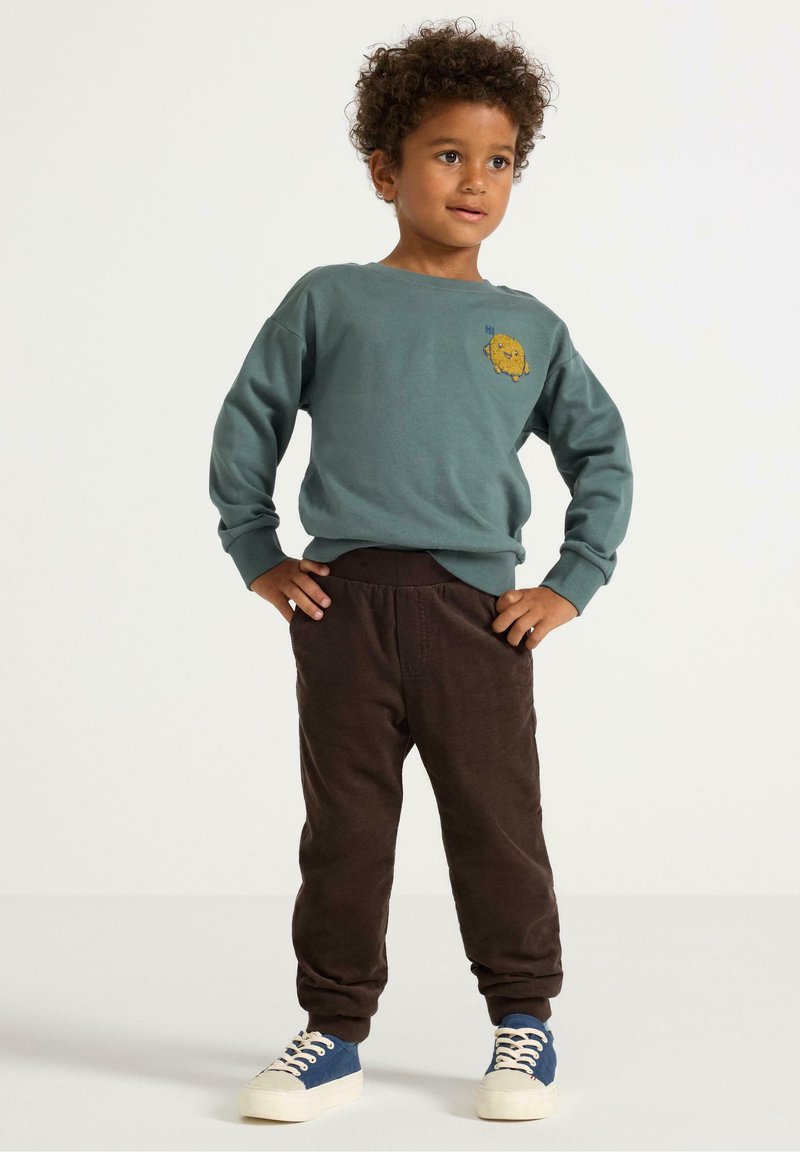Grøn bomulds sweatshirt med et gult broderet grafik, parret med brune kordfløjl bukser og blå sneakers med hvide snørebånd.